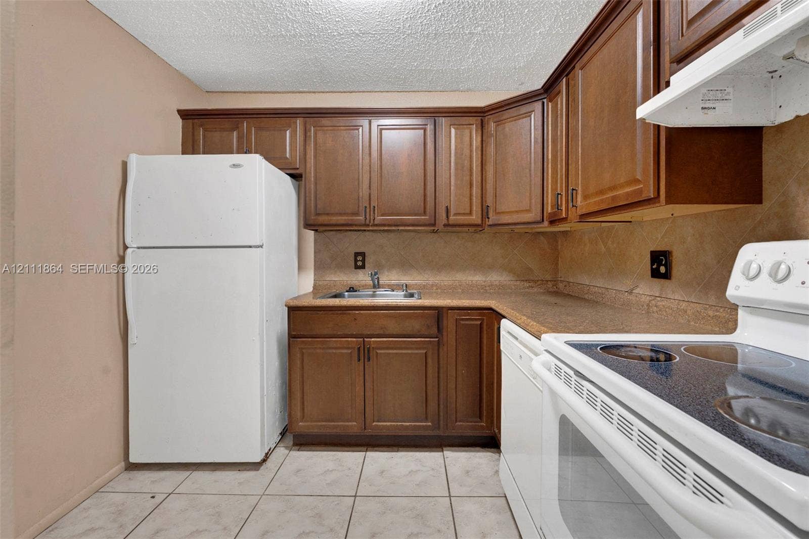 6195 Rock Island Road, #104, Tamarac, FL 33319 Kitchen featuring wood cabinetry, stone-texture tile backsplash, laminate countertops, and tile flooring