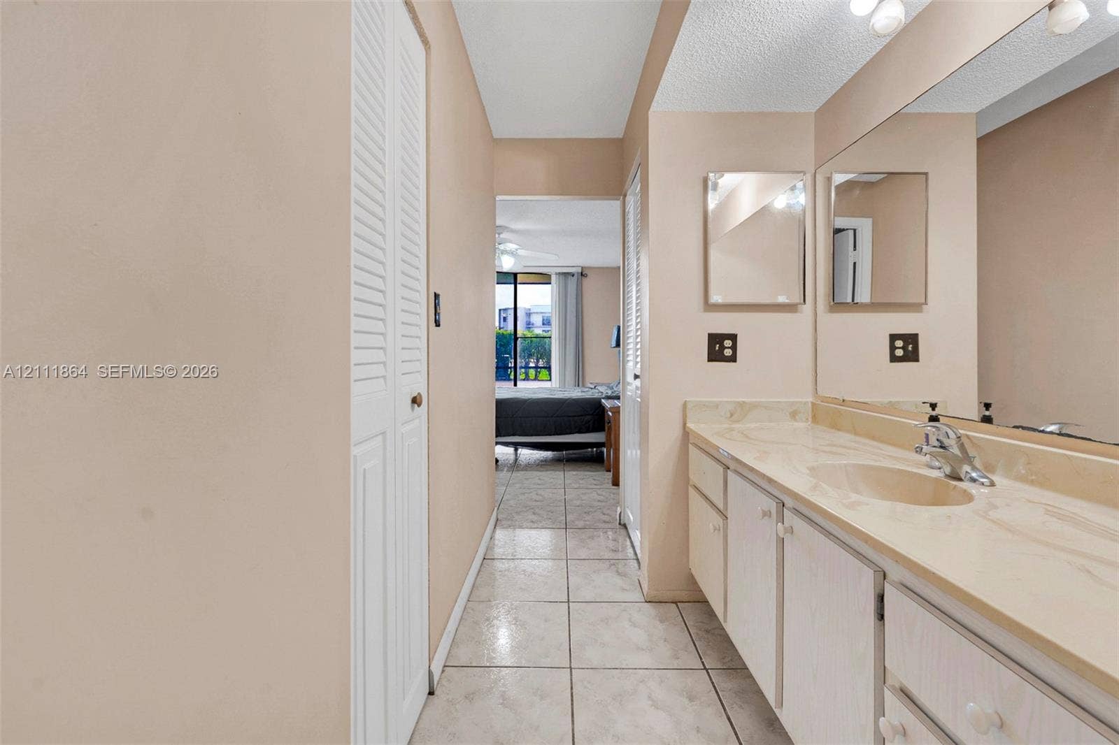 6195 Rock Island Road, #104, Tamarac, FL 33319 Bathroom featuring a long vanity with an integrated basin, light-toned cabinetry, a full-width mirror, tile flooring, and louvered closet doors