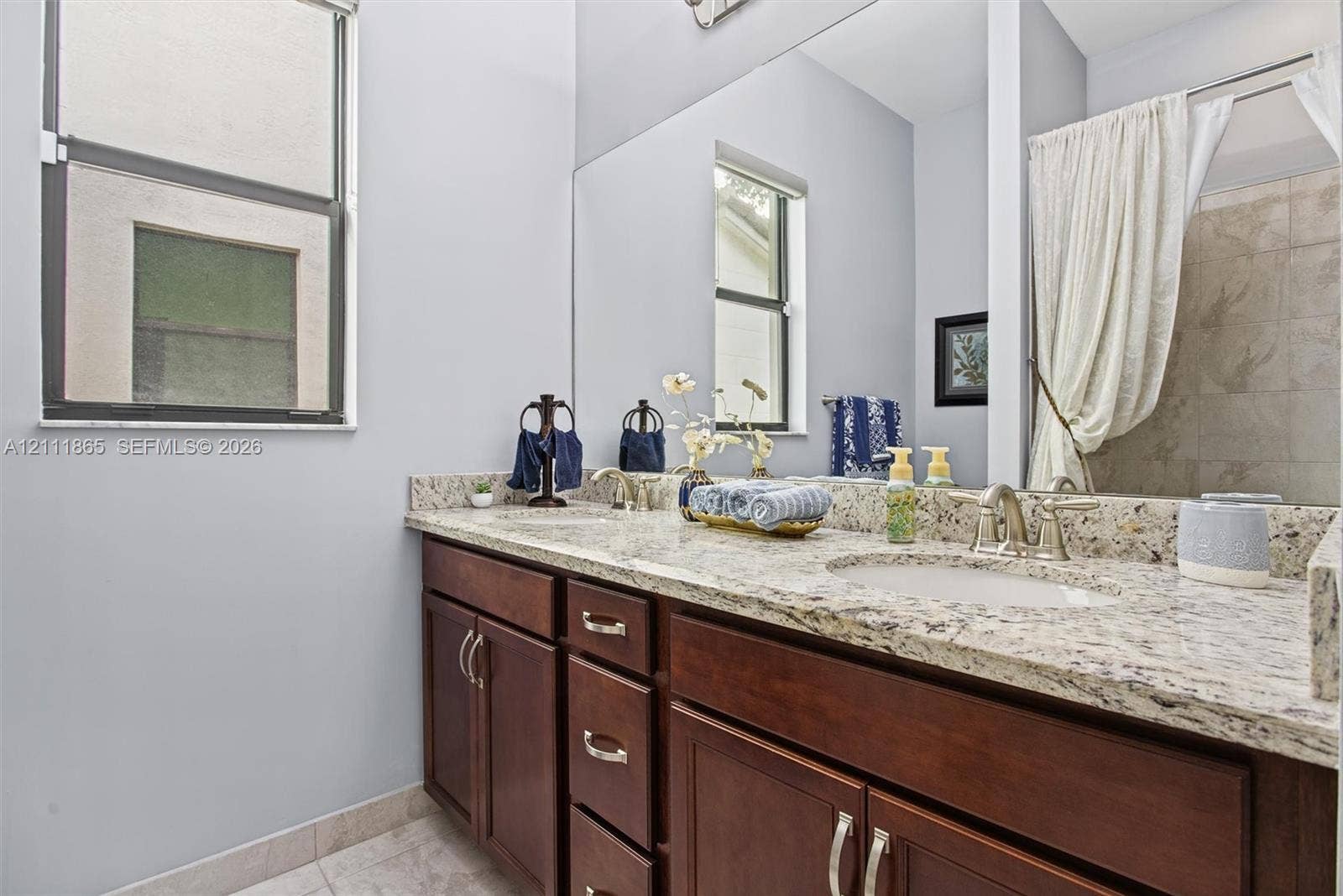 1034 SW 113th Avenue, Pembroke Pines, FL 33025 Second bathroom featuring a dual-sink vanity with stone countertops, rich wood-finish cabinetry & large wall-mounted mirror.