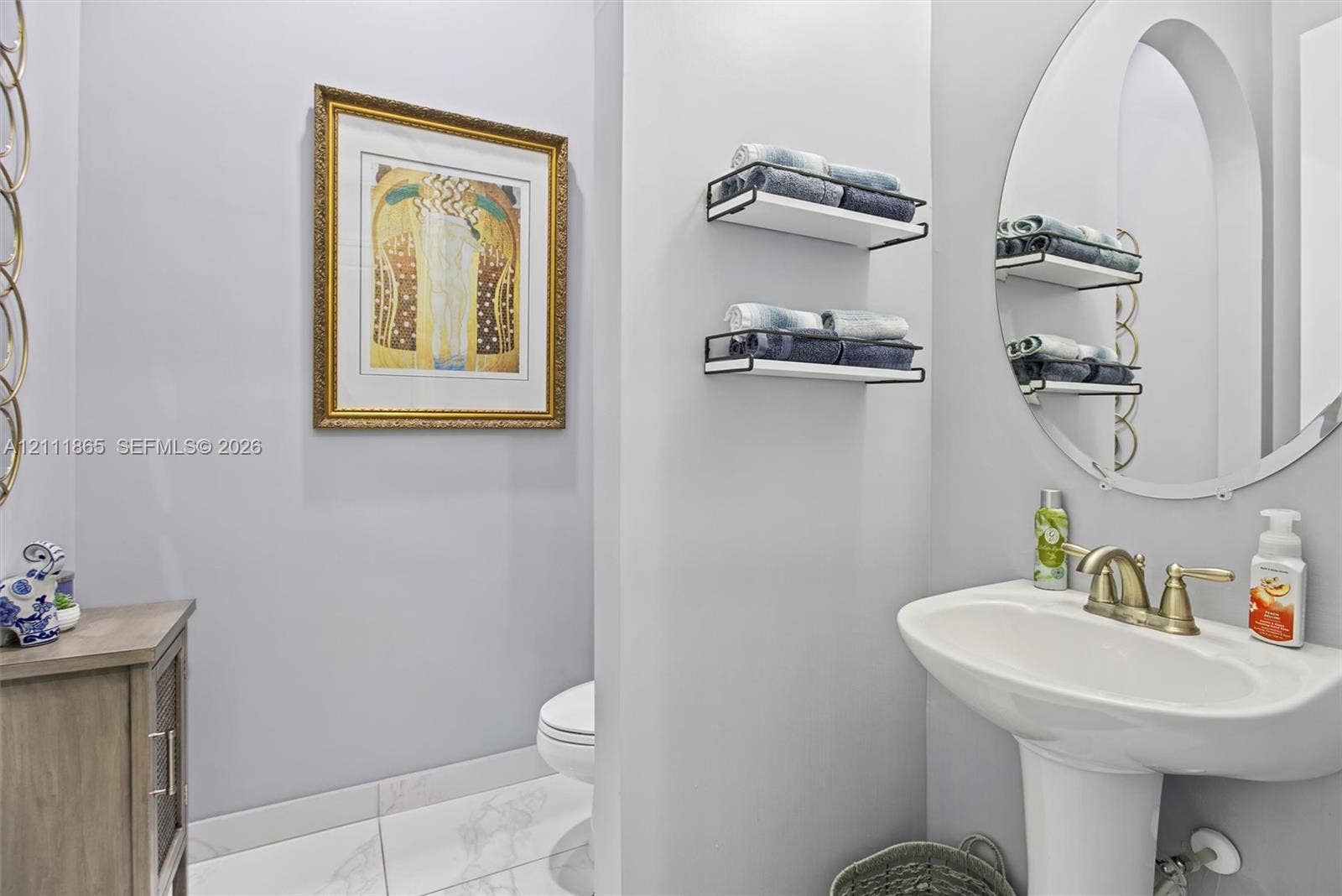 1034 SW 113th Avenue, Pembroke Pines, FL 33025 Chique powder room featuring white pedestal sink, metallic finish faucet, oval mirror & wall-mounted shelving.