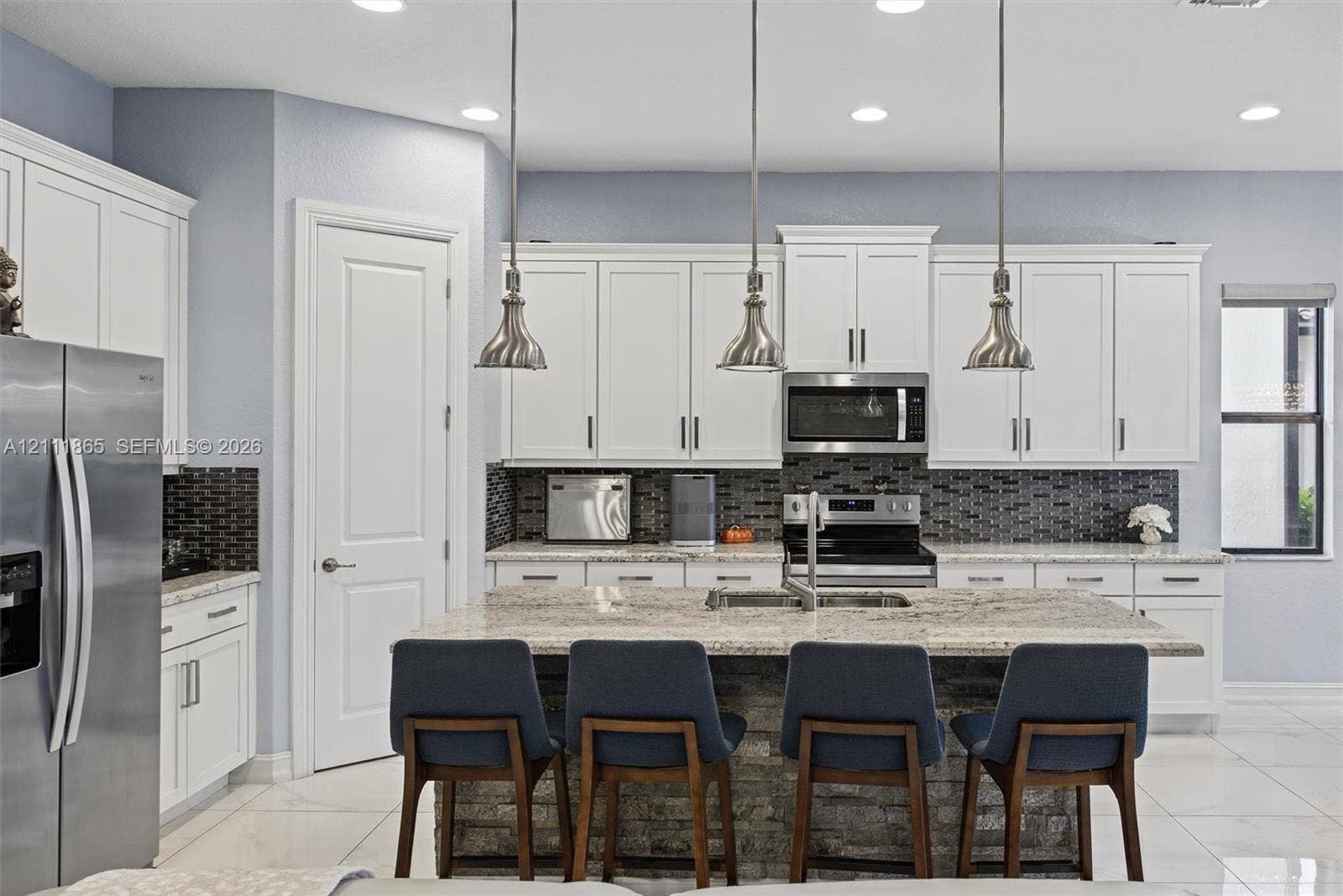 1034 SW 113th Avenue, Pembroke Pines, FL 33025 Beautiful kitchen featuring white shaker-style cabinetry, & stone-surface center island & stylish over counter pendant lighting.