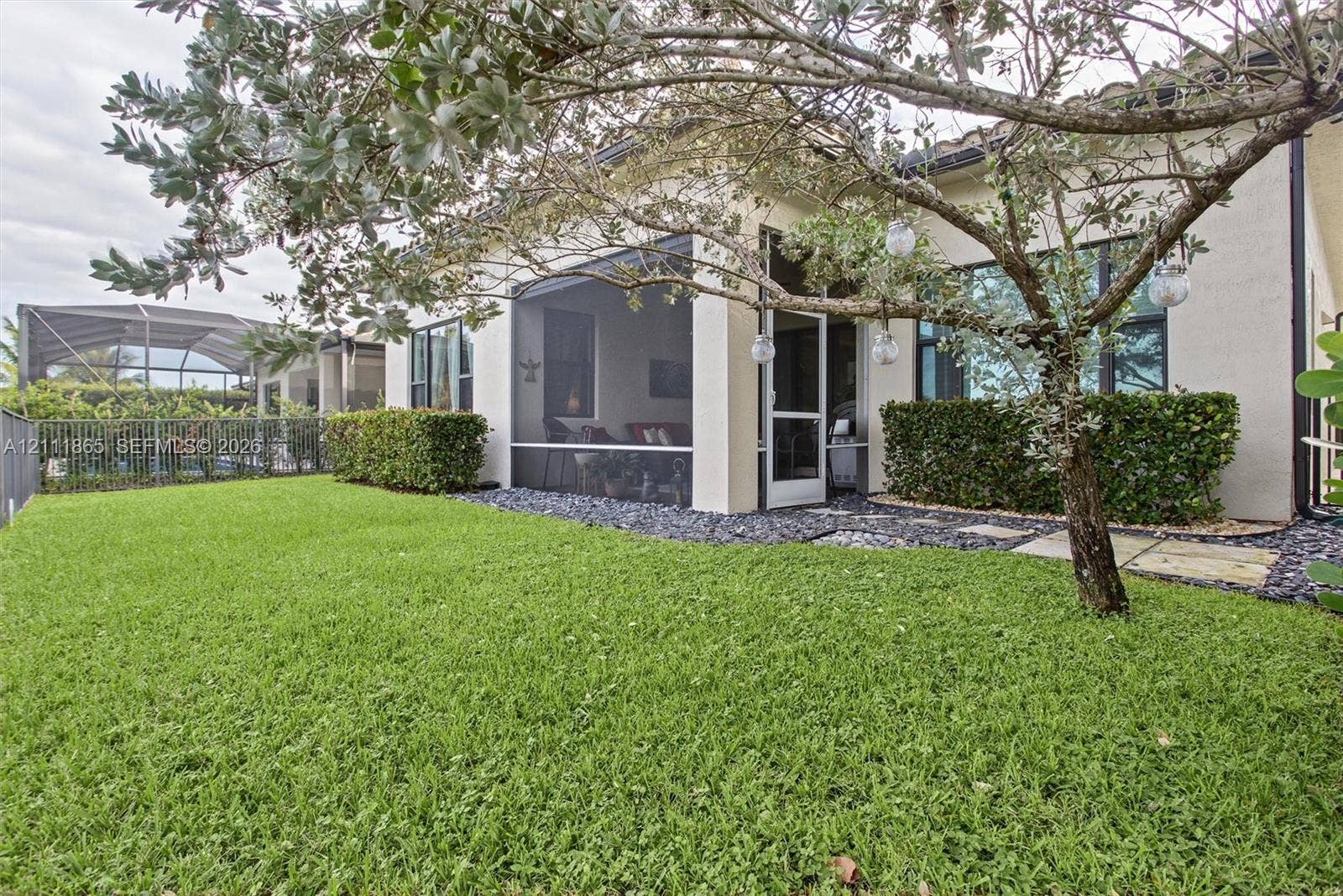 1034 SW 113th Avenue, Pembroke Pines, FL 33025 Back yard perspective. Notice lawn, dark stone landscape border, and shade tree