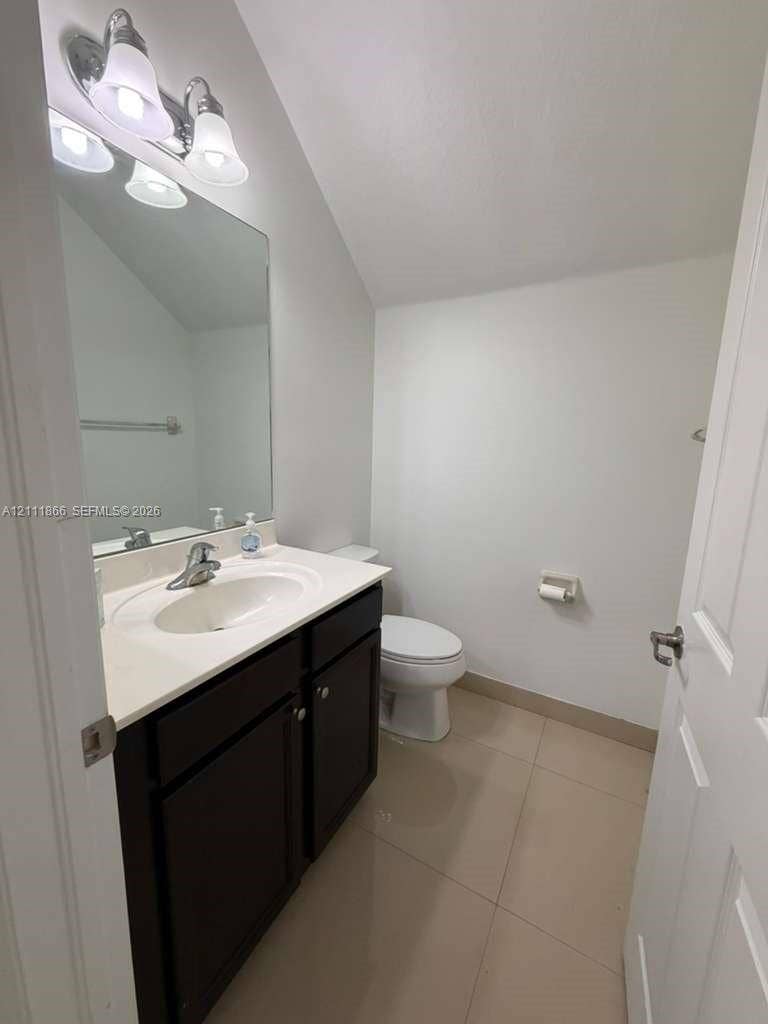 Bathroom featuring a vanity with dark cabinetry, solid-surface countertop, integrated oval sink, full-width wall mirror, and dual-bulb vanity light