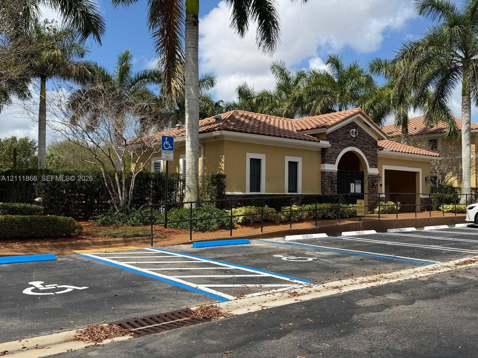 Stucco exterior featuring stone veneer accents, terra-cotta tile roofing, arched entryway, and landscaped grounds with mature palm trees