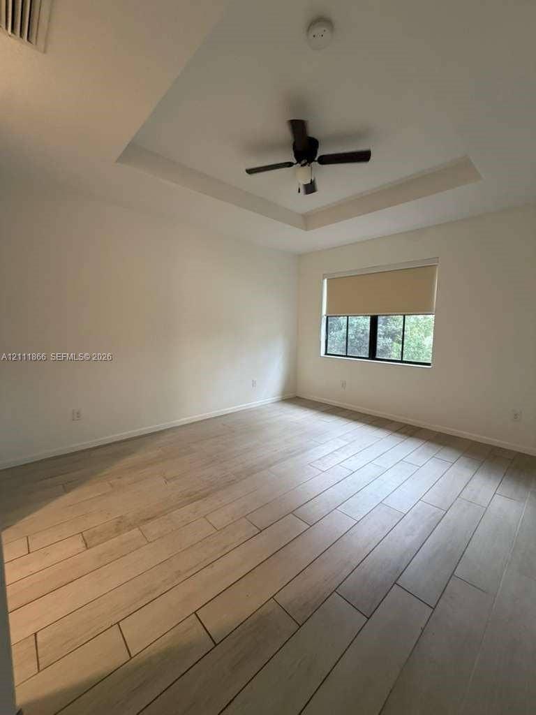 Room featuring a tray ceiling, ceiling fan with integrated lighting, window with a roller shade, and wood-finish tile flooring