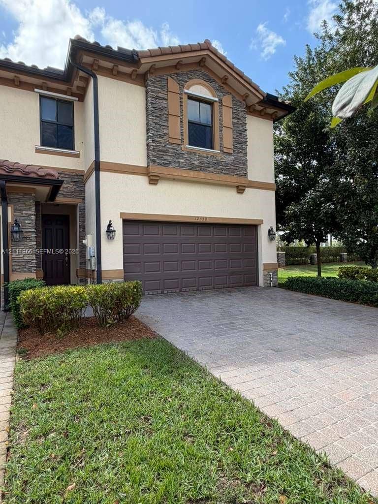 Two-story exterior featuring a stone facade, stucco siding, a tiled roof, a paved driveway, and wall-mounted exterior lighting