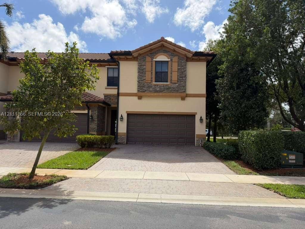 Stucco exterior with stone veneer accents, multi-paned window detailing, tile roofing, and a paved driveway leading to an attached two-car garage