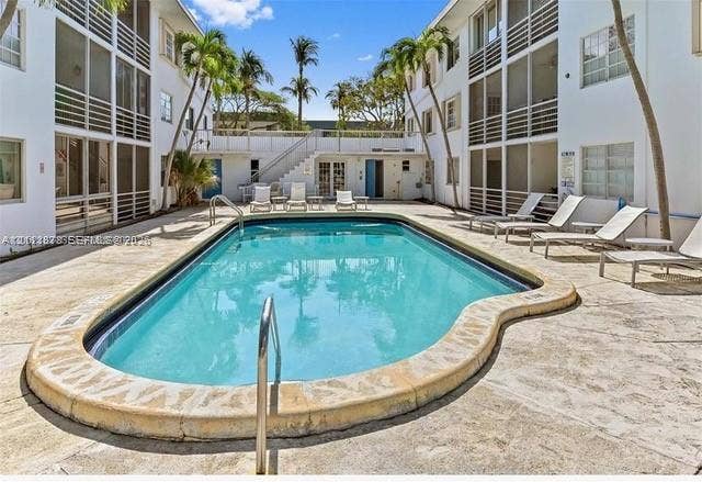 201 Galen Drive, #110, Key Biscayne, FL 33149 In-ground swimming pool featuring a curved concrete coping, surrounded by a stone paver deck, palm trees, and multi-story structures with screened enclosures