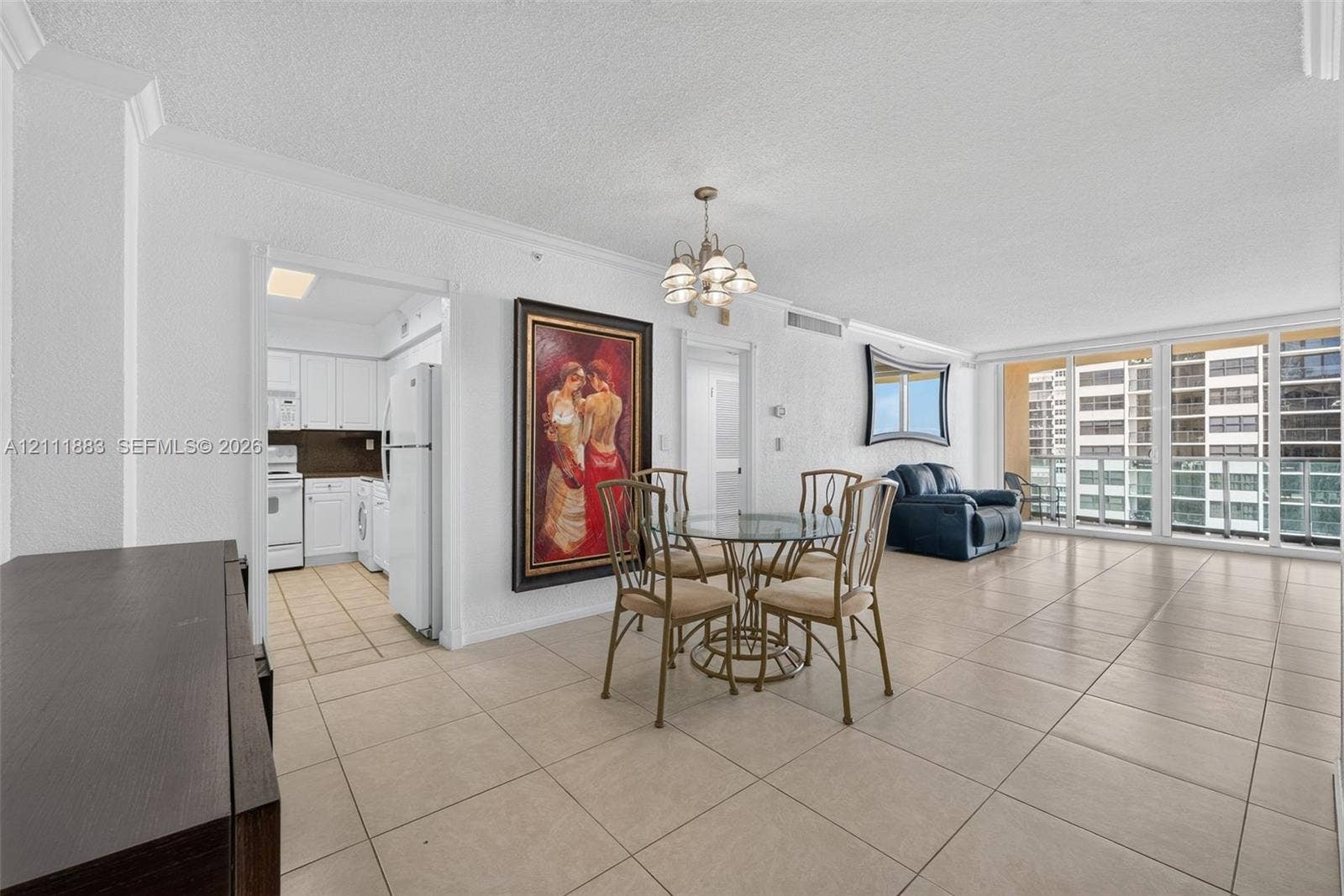 Open-concept interior featuring large-format ceramic tile flooring, a multi-light chandelier, floor-to-ceiling glass sliding doors, and crown molding