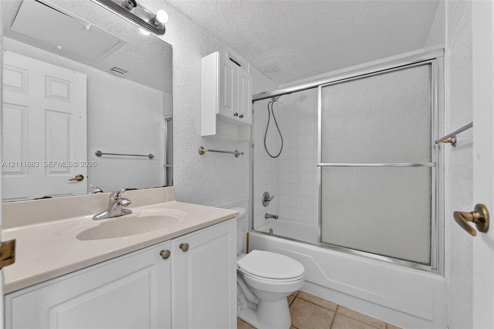 Bathroom featuring a white vanity cabinet with an integrated basin, wall-mounted storage cabinetry, a large vanity mirror with overhead lighting, and a tub-shower combination with sliding glass doors