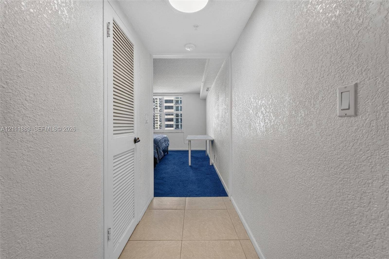 Hallway featuring large-format ceramic tile flooring, textured wall surfaces, and a full-height louvered door closet