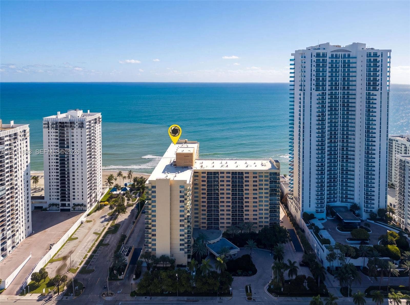 High-rise residential building featuring expansive ocean frontage, private balconies, structured parking, and palm tree-lined landscaping