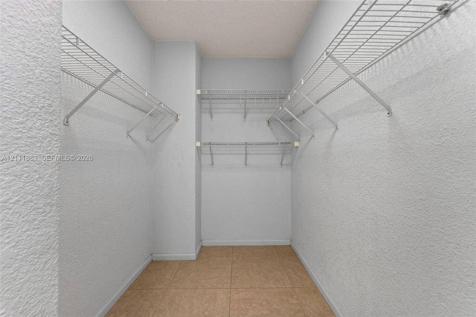 Walk-in storage space featuring ceramic tile flooring, textured wall finishes, and tiered wire shelving