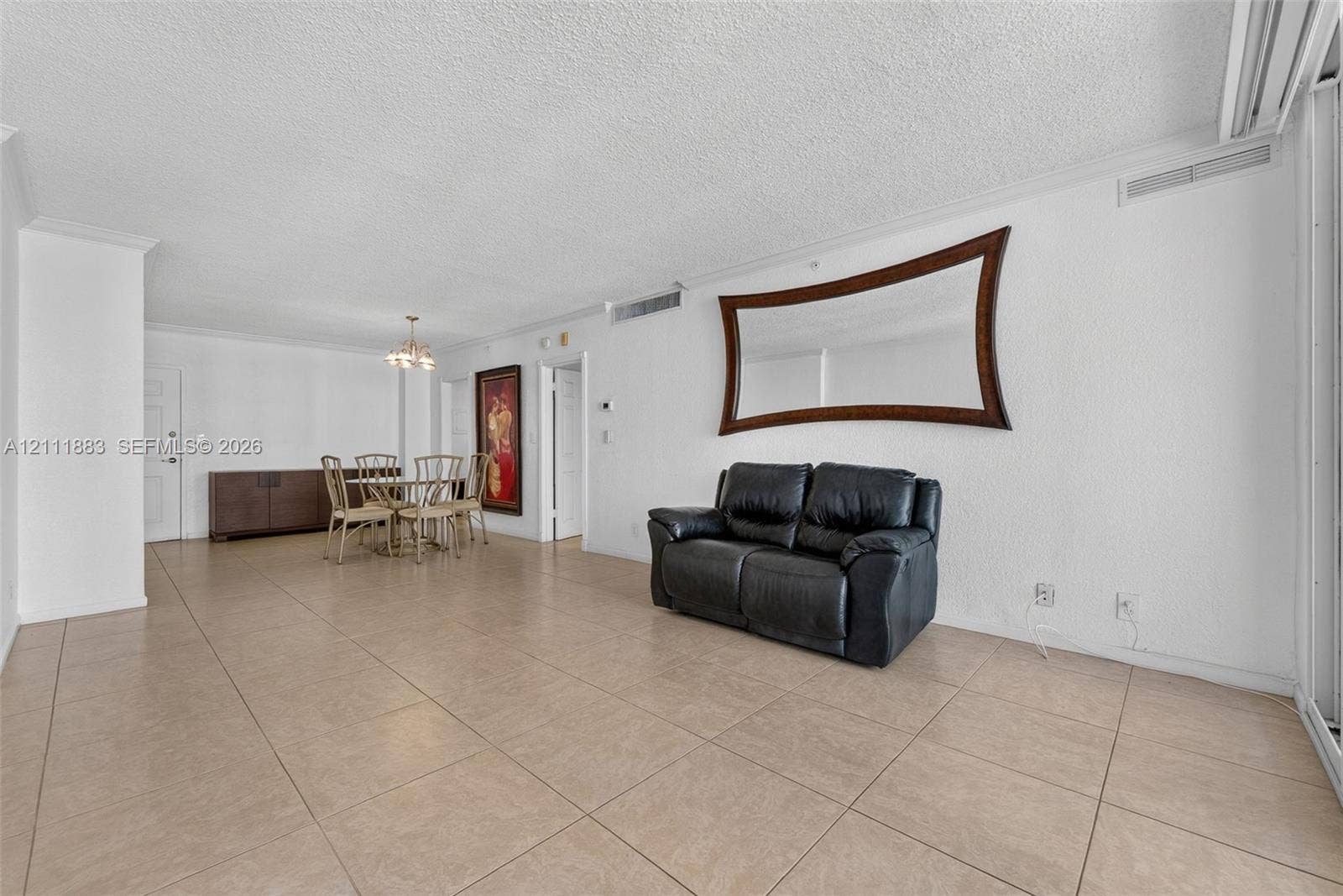 Open floor plan featuring neutral large-format tile flooring, textured ceiling, and a wall-mounted decorative wood-frame mirror