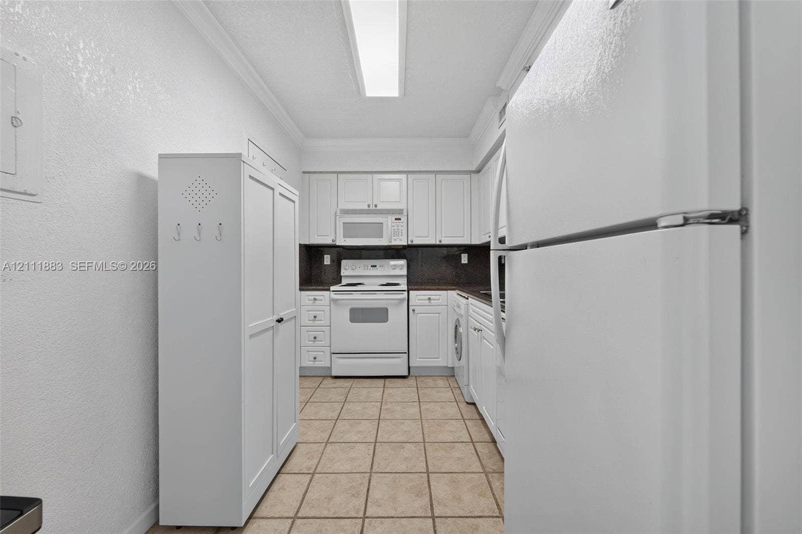Kitchen featuring white cabinetry, tile flooring, integrated white appliances, and linear ceiling lighting