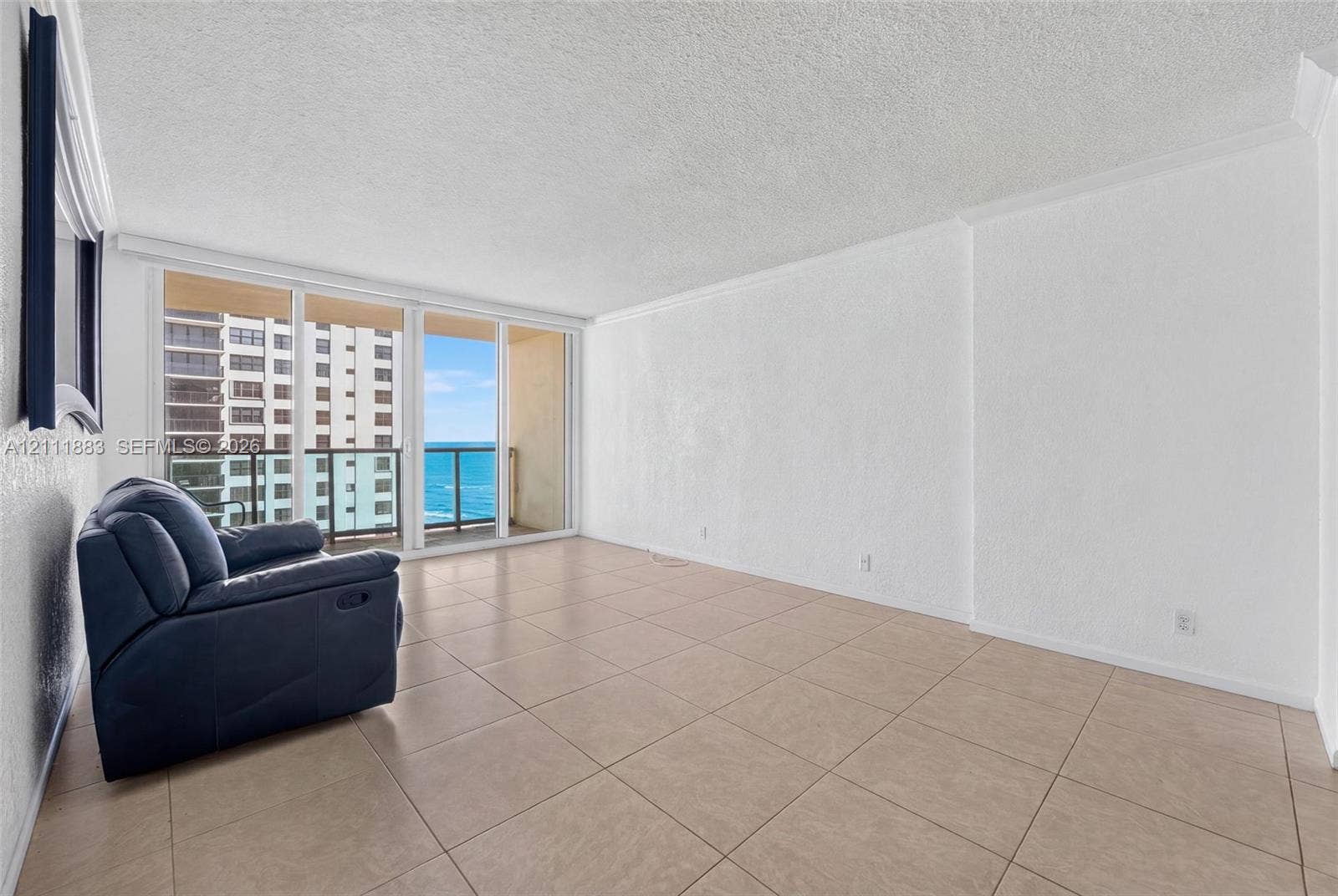 Open-concept room featuring oversized neutral floor tile, textured wall finishes, and floor-to-ceiling glass sliding doors opening to an exterior balcony