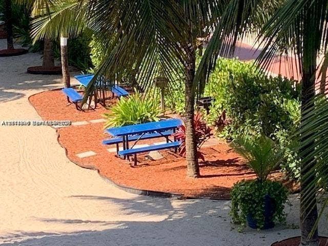 Outdoor common area featuring sand surfacing, mulched landscaping beds, mature palm trees, and built-in metal grills
