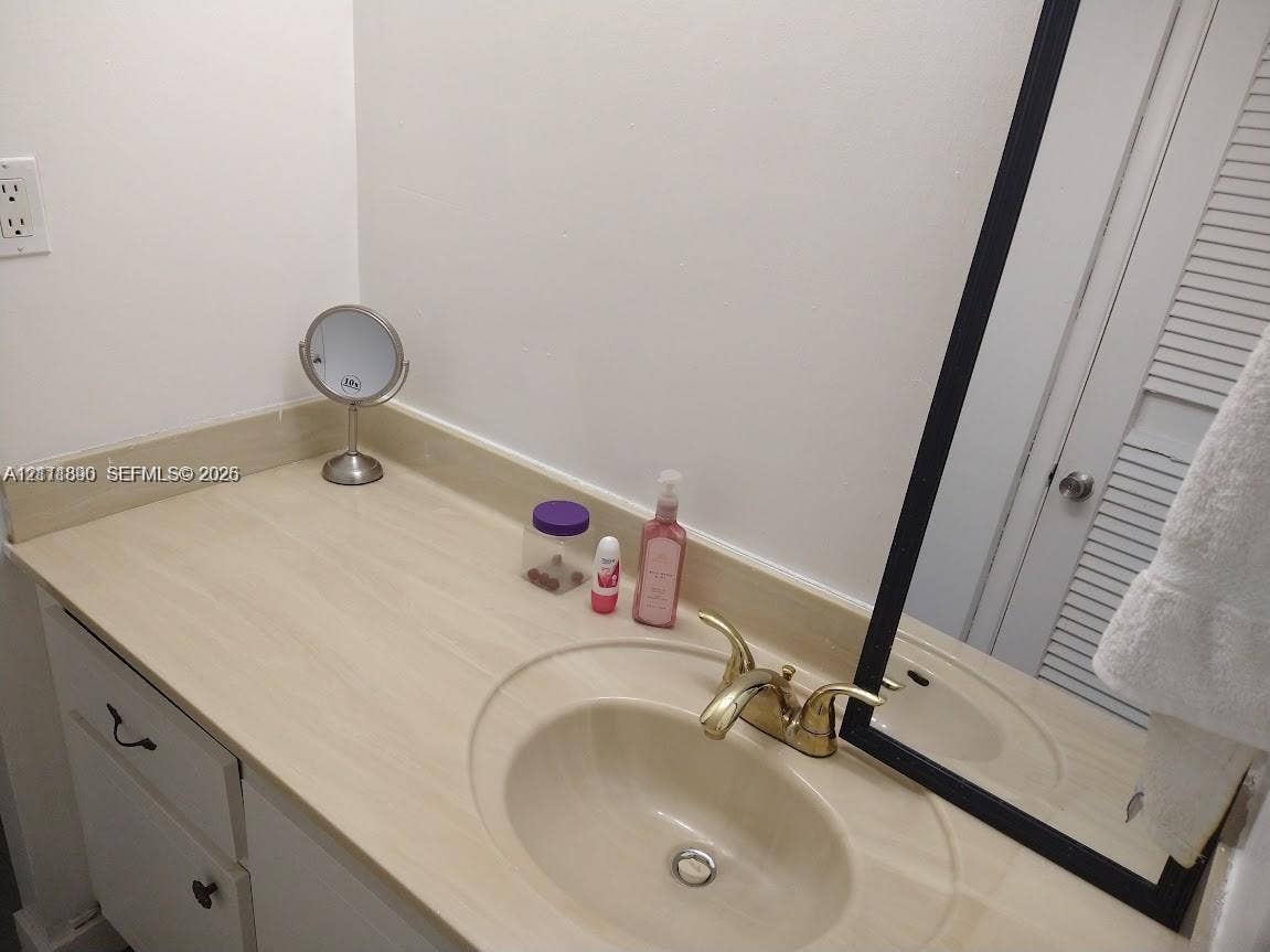 Bathroom vanity featuring a solid-surface countertop with an integrated basin, brass-finish double-handle faucet, white cabinetry, and a rectangular mirror with a black frame
