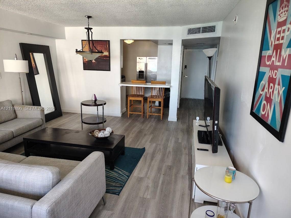 Open-concept floor plan featuring wood-finish flooring, a built-in breakfast bar, and a hanging metal chandelier