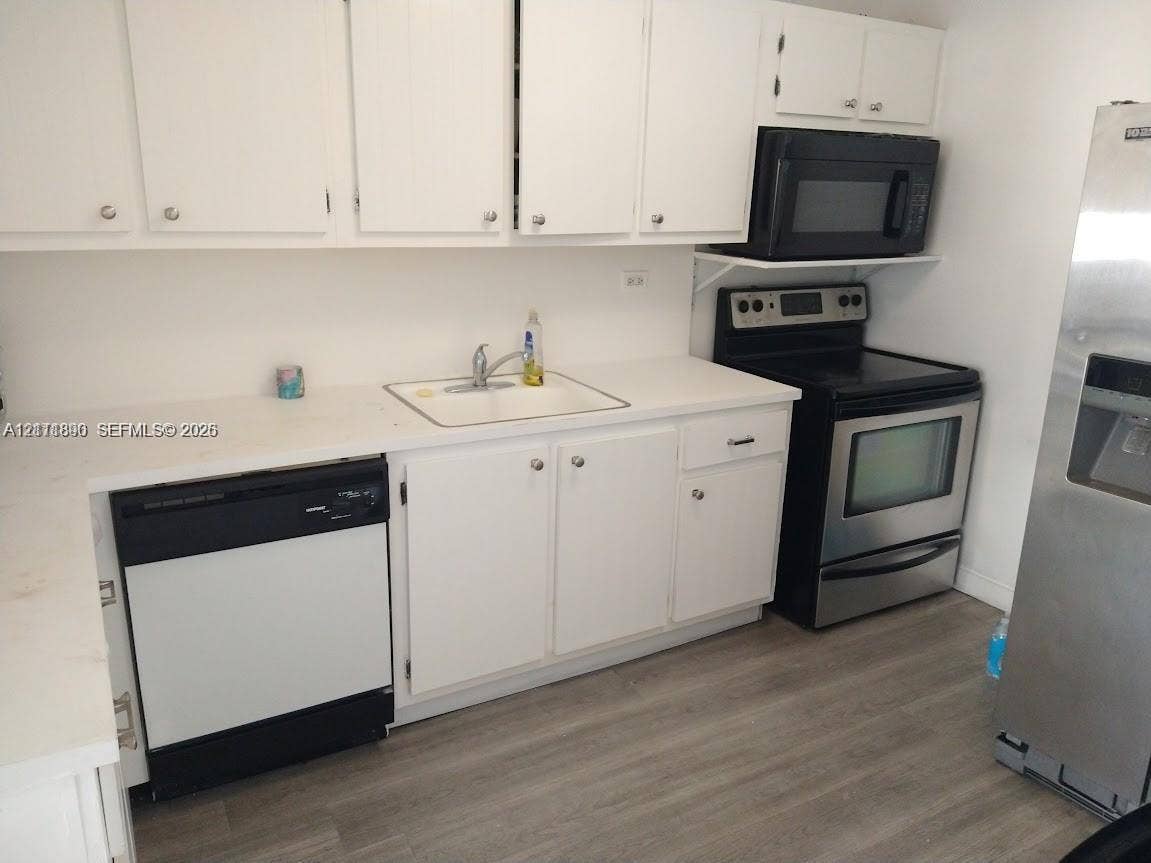 Kitchen featuring white cabinetry, wood-finish flooring, and a suite of stainless steel and black appliances including a range, microwave, and dishwasher