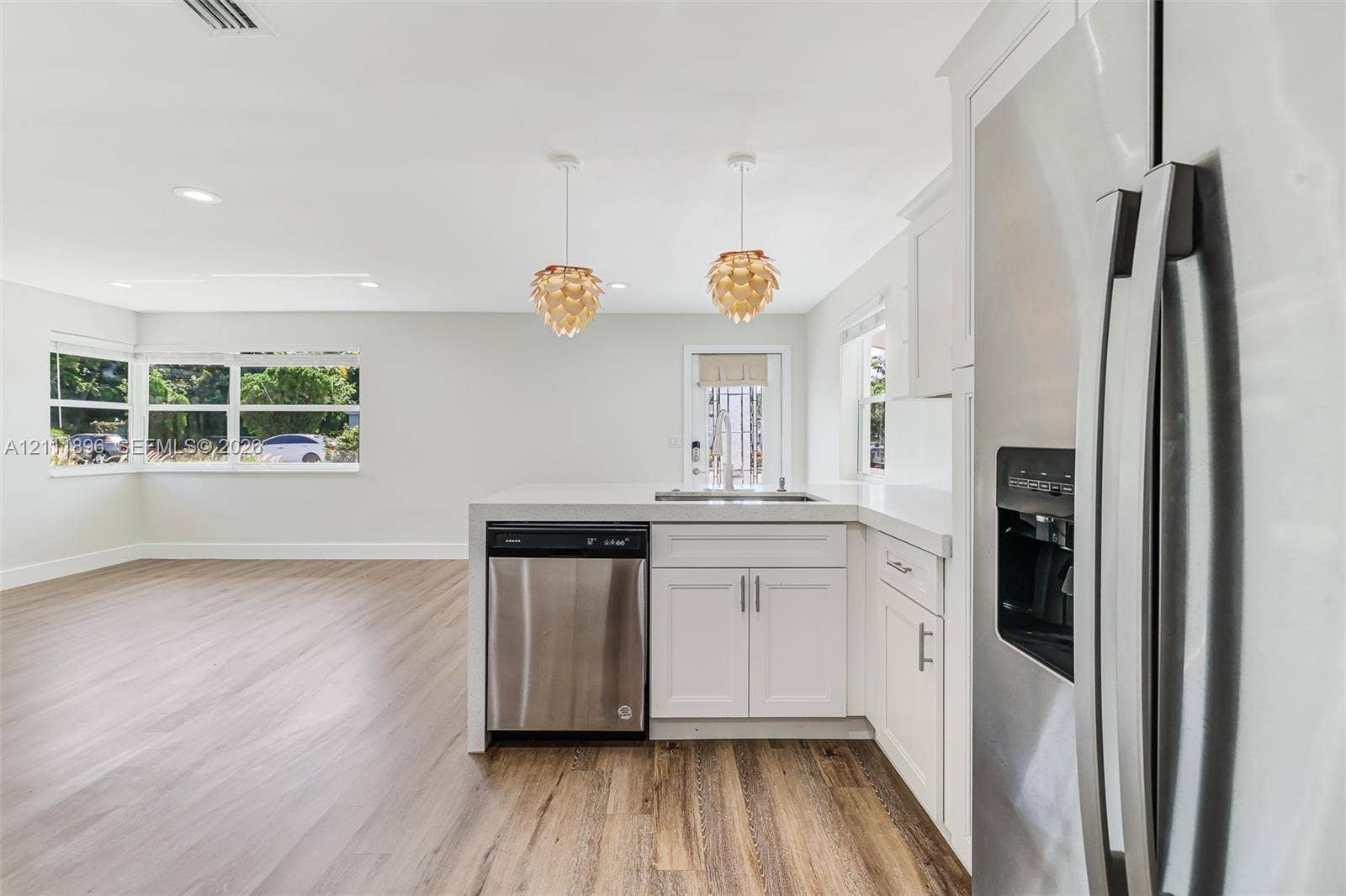 Kitchen featuring white cabinetry, stainless steel appliances, wood-finish flooring, stone-style countertops, and pendant lighting