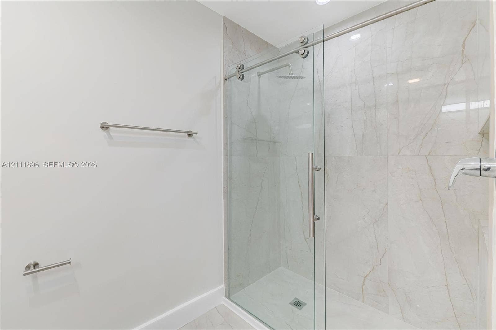 Walk-in shower featuring large-format tile surround, frameless glass sliding door, rainfall showerhead, and wall-mounted brushed metal fixtures