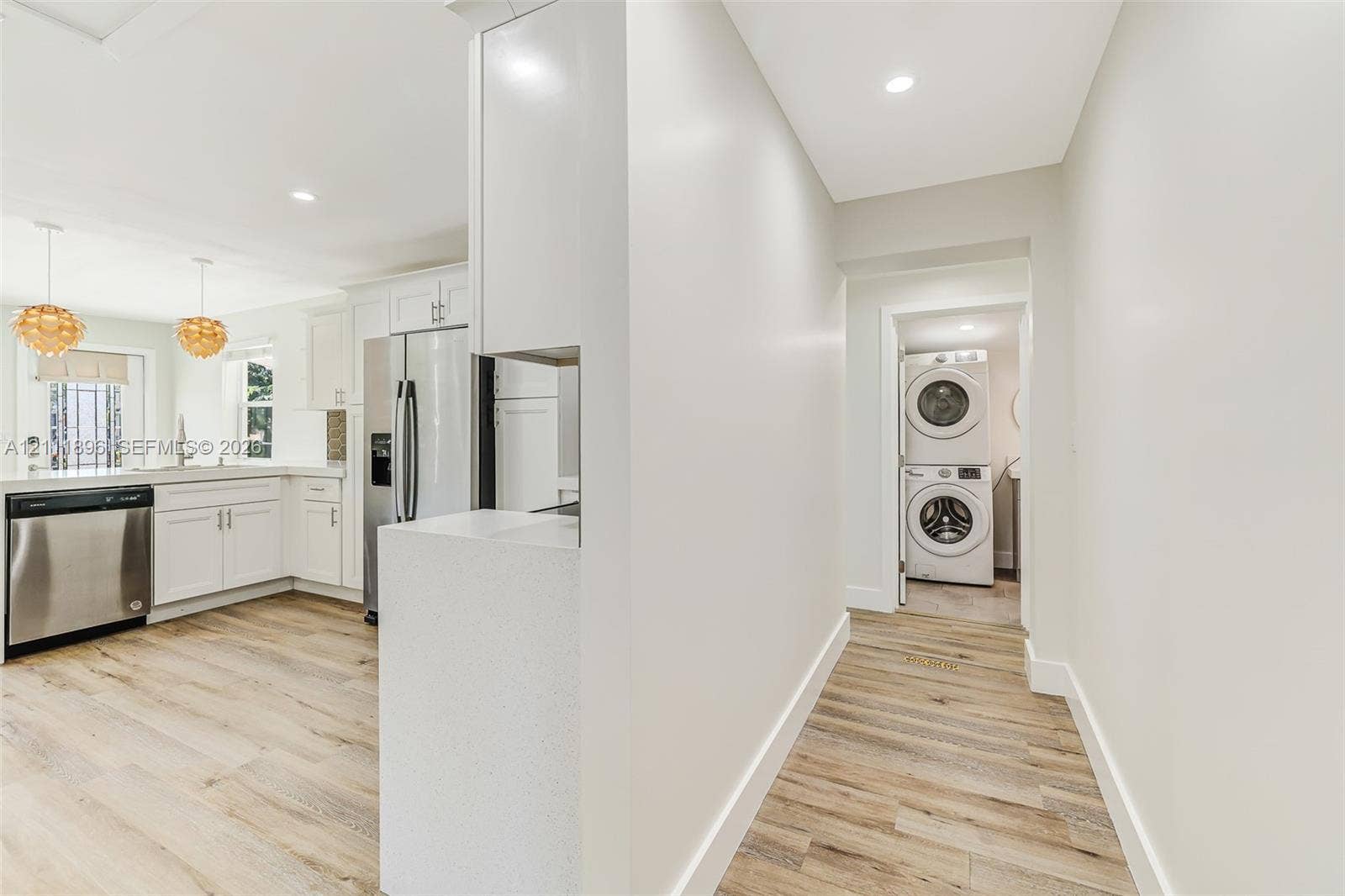 Kitchen featuring white shaker-style cabinetry, stainless steel appliances, and wood-finish flooring, complemented by a laundry area with a stacked washer and dryer