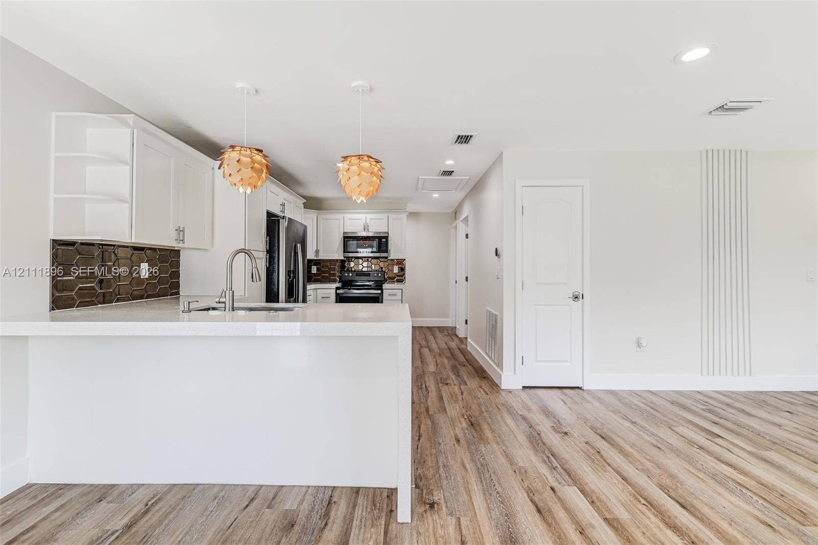 Kitchen featuring white cabinetry, wood-finish flooring, geometric tile backsplash, quartz-style countertops, and pendant lighting