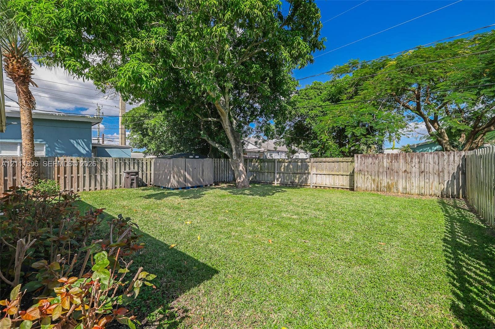 Fenced backyard featuring a manicured lawn, mature trees, and landscaping