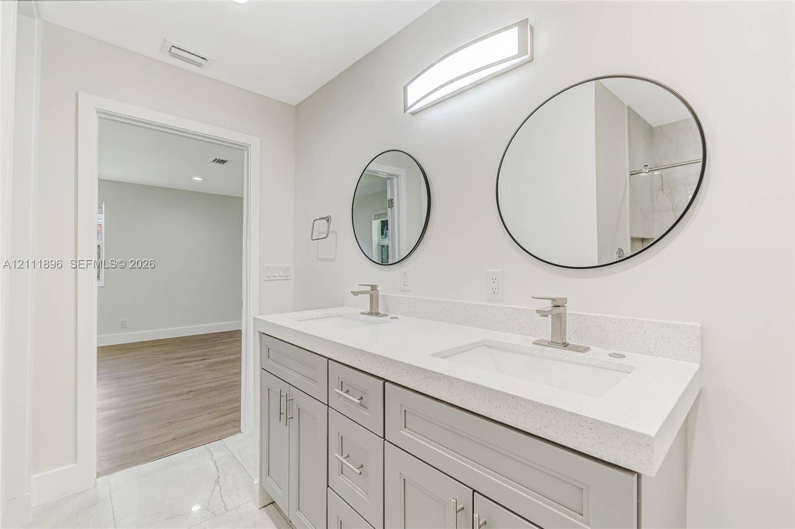 Double vanity featuring gray shaker-style cabinetry, a stone-composite countertop, integrated rectangular sinks, brushed-nickel faucets, and dual circular mirrors