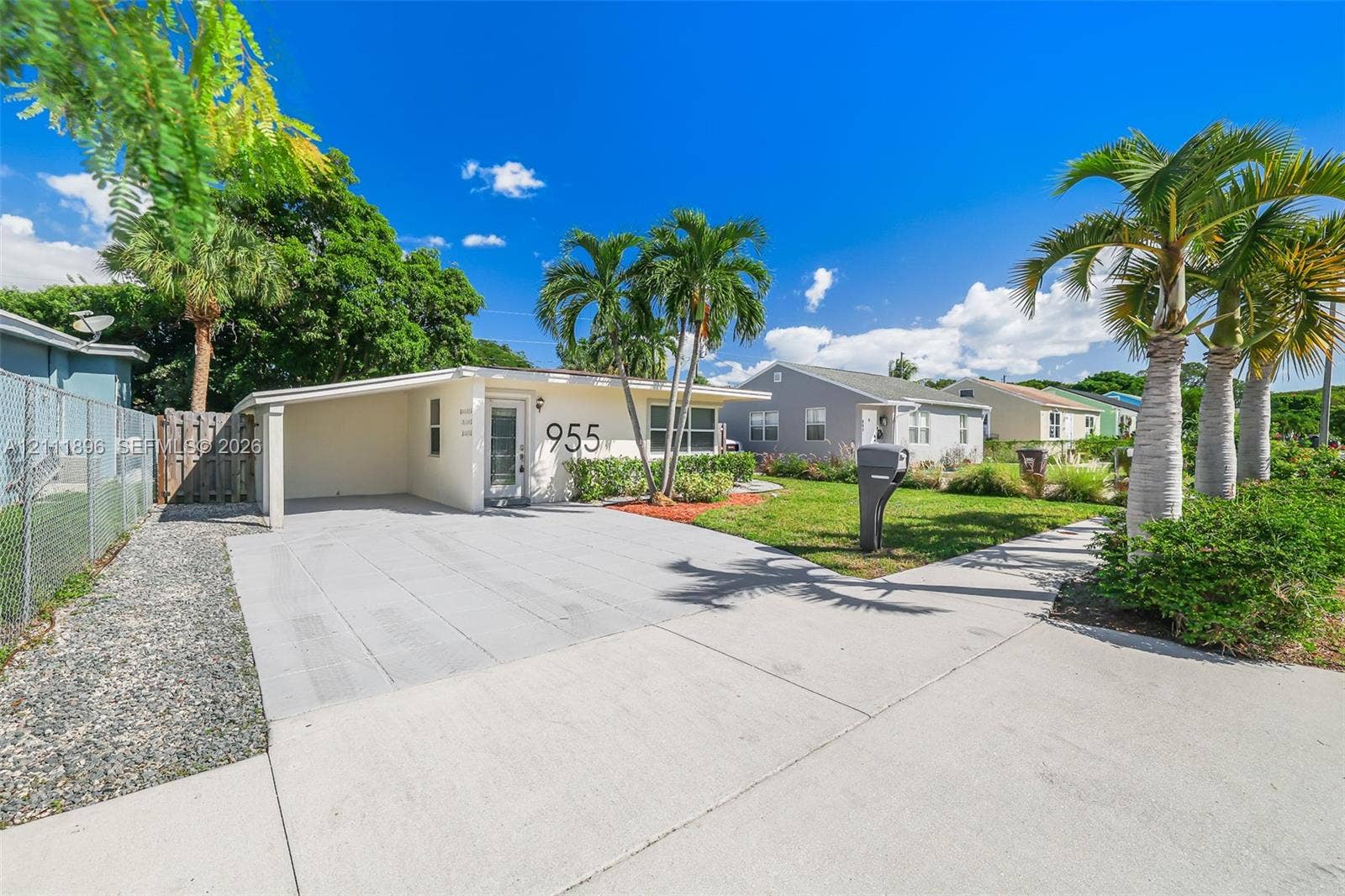 Single-story exterior featuring a covered carport, concrete driveway, front lawn, and mature palm trees