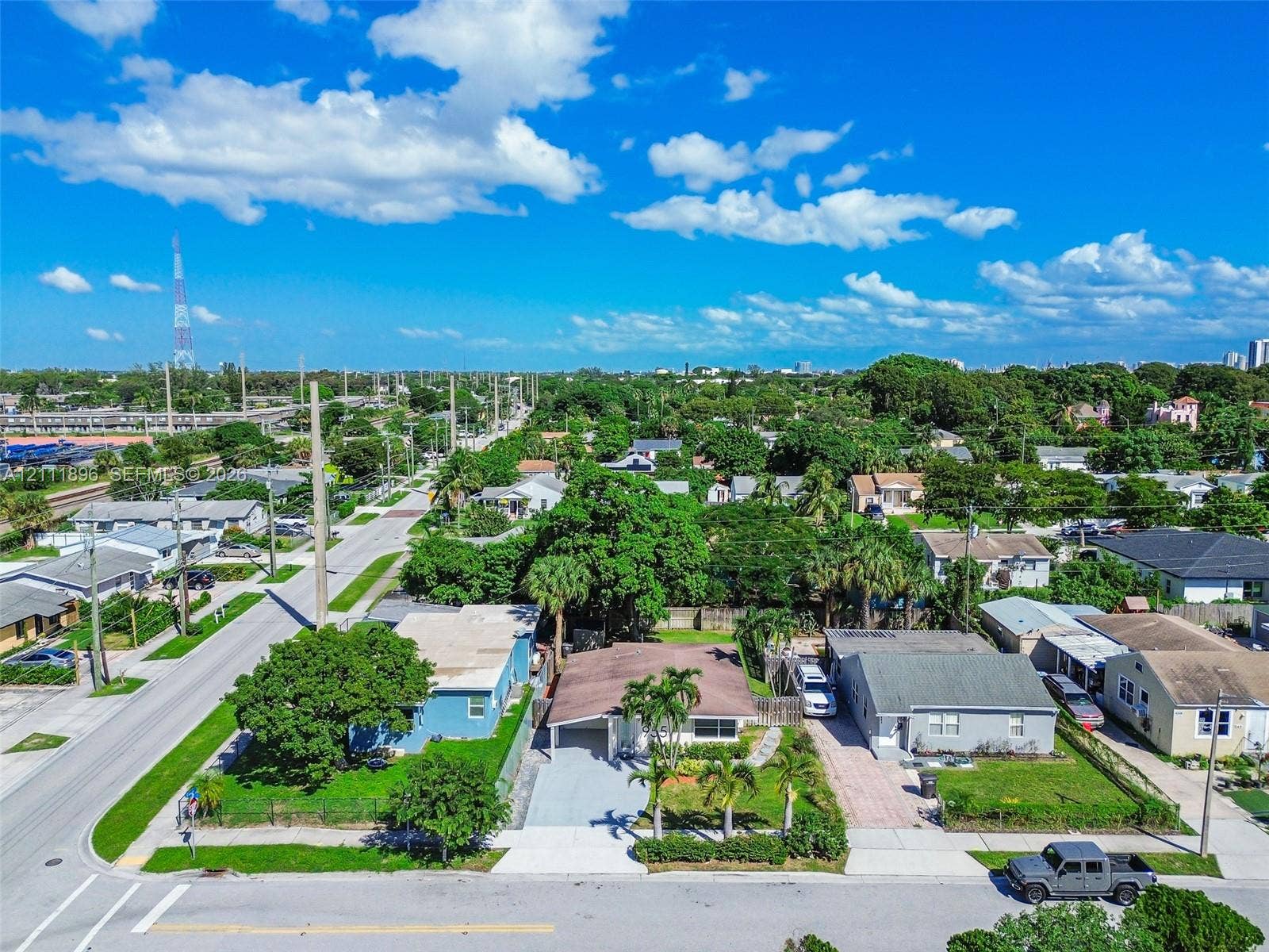Aerial view of a residential property featuring a paved driveway, covered entryway, and mature palm trees