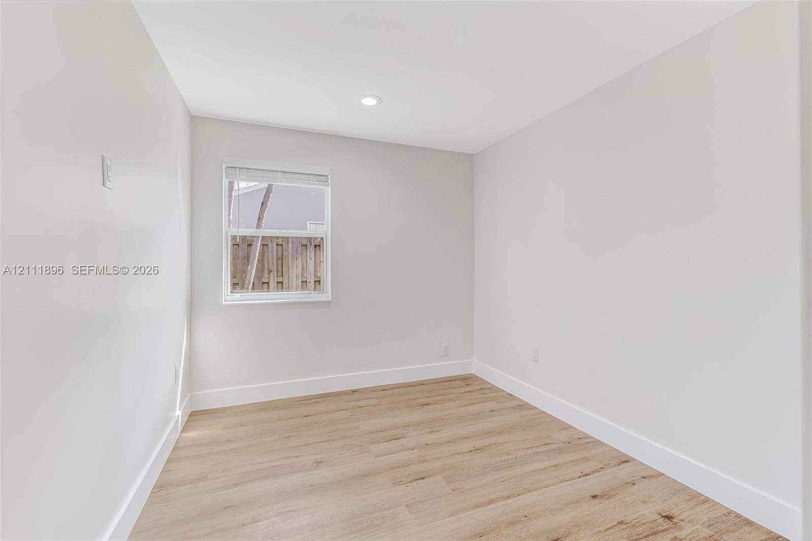 Neutral-toned interior featuring wood-finish flooring, a single window, and a recessed ceiling light