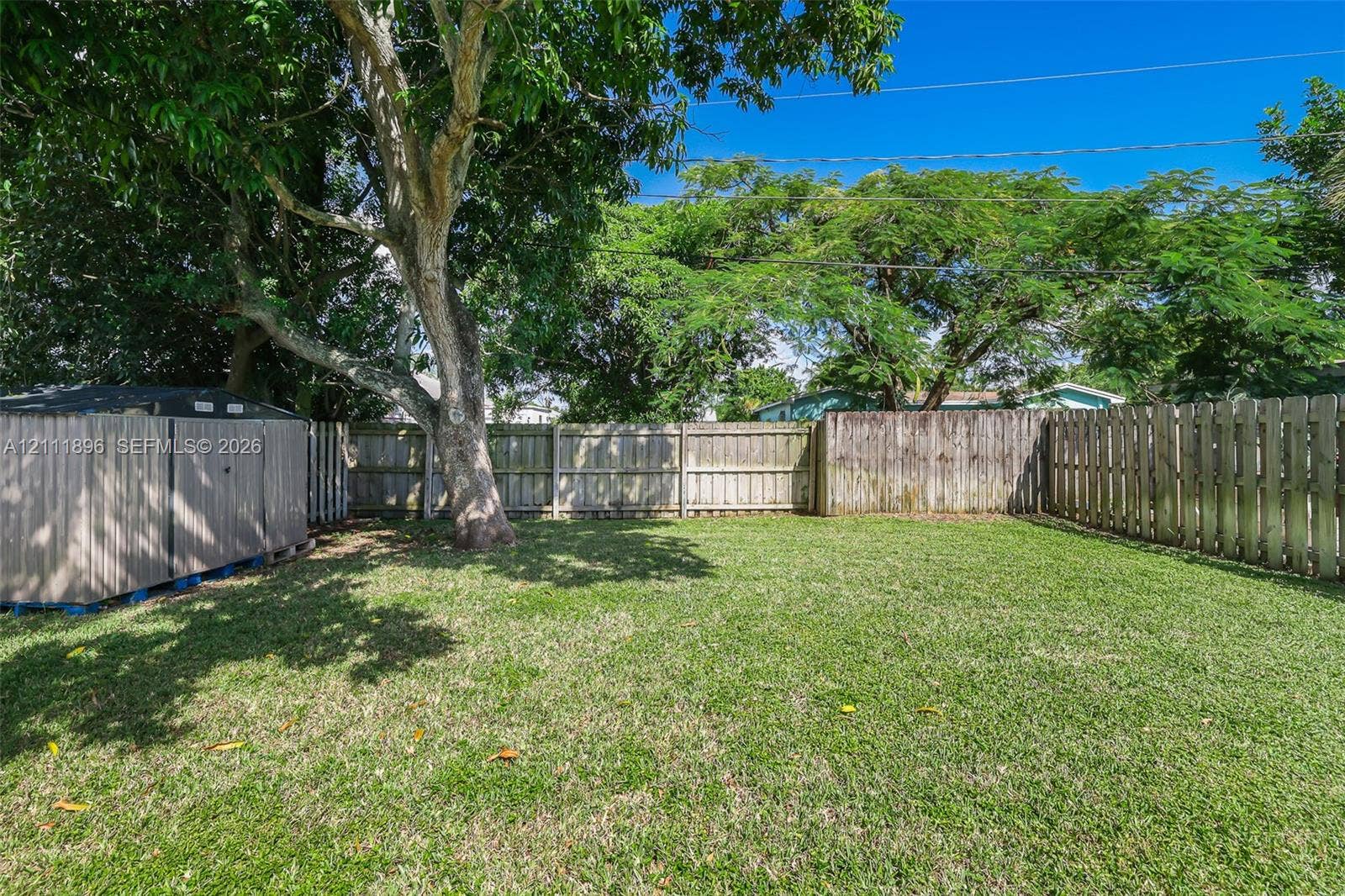 Private backyard featuring a manicured lawn, full-perimeter wood fencing, and mature canopy trees