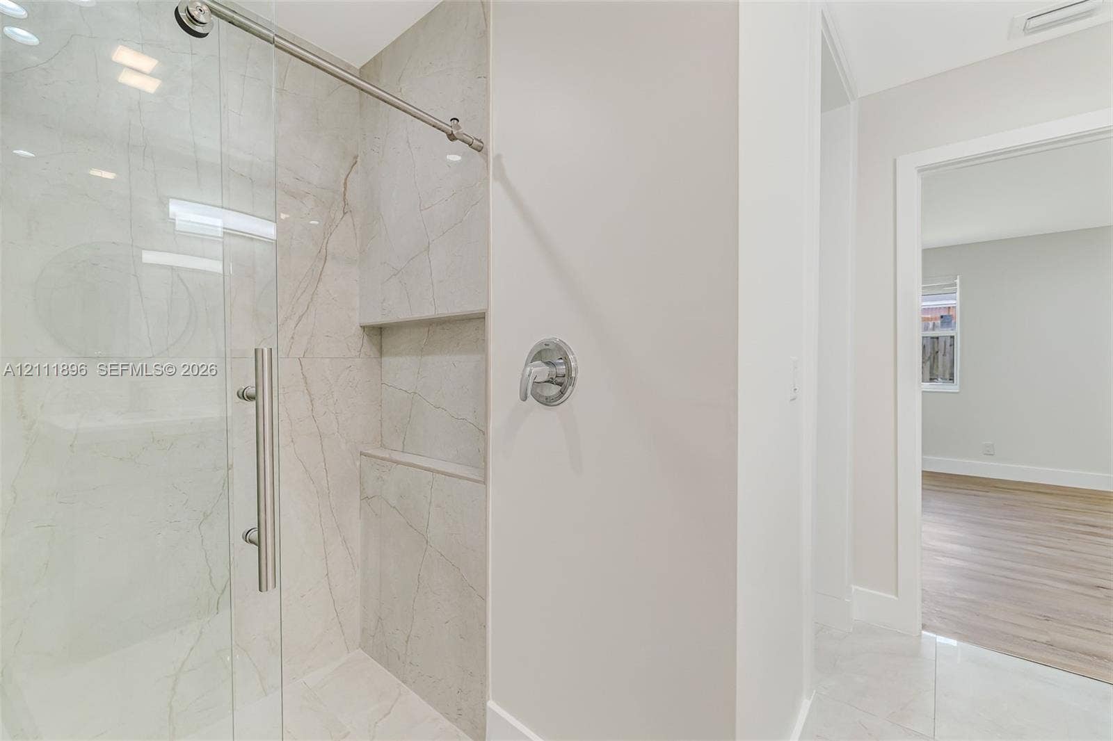 Walk-in shower featuring large-format stone-finish tile surround, a built-in recessed niche, chrome hardware, and a frameless glass enclosure