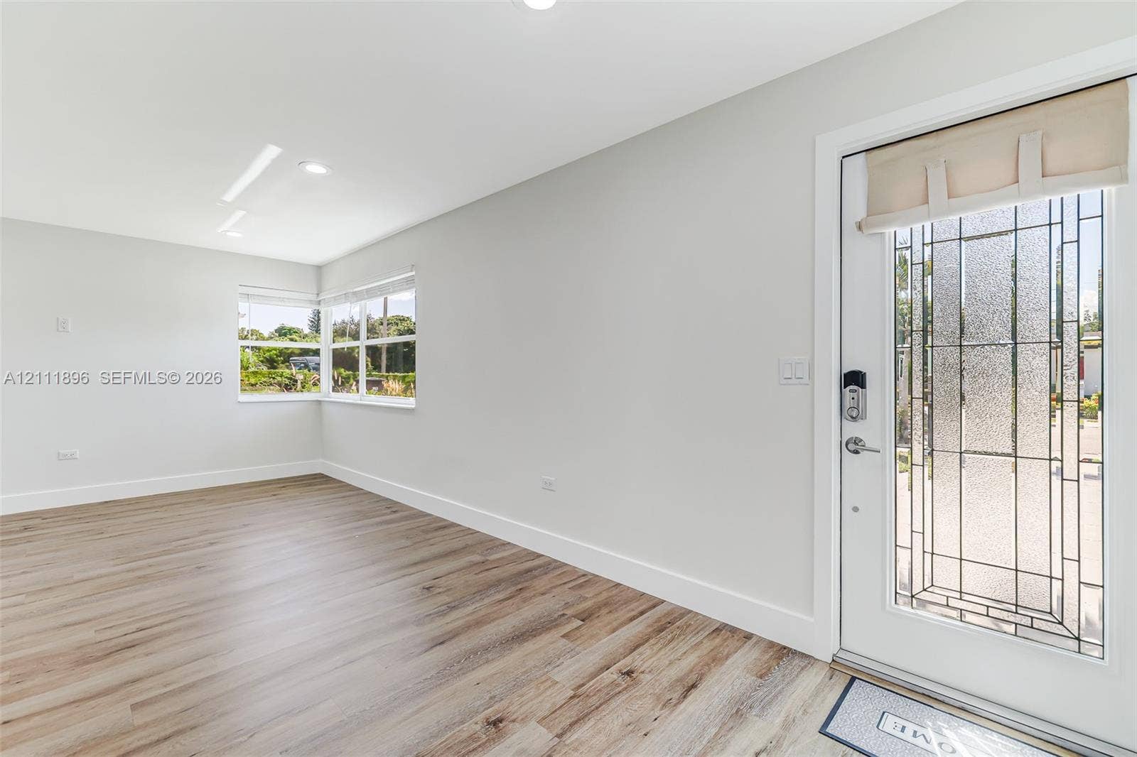 Neutral-toned interior featuring wood-finish flooring, recessed lighting, and a front entry door with a decorative glass insert
