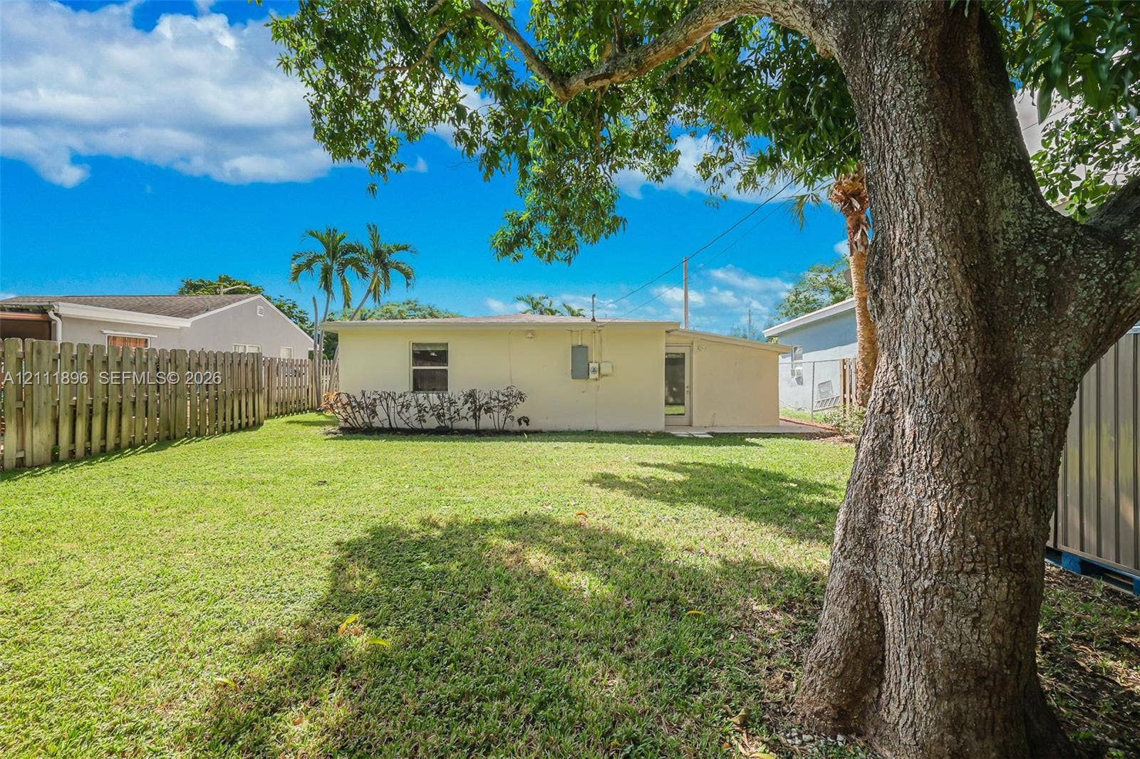 Backyard featuring a grass lawn, mature tree, and wood-panel privacy fencing
