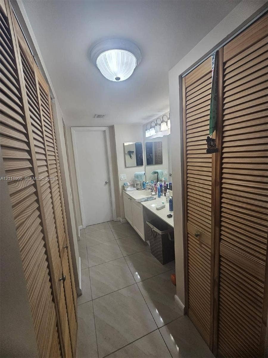 711 N Pine Island Road, #402, Plantation, Plantation, FL 33324 Dual louvered-door closets, tile flooring, vanity with integrated cabinetry, and multi-bulb wall lighting