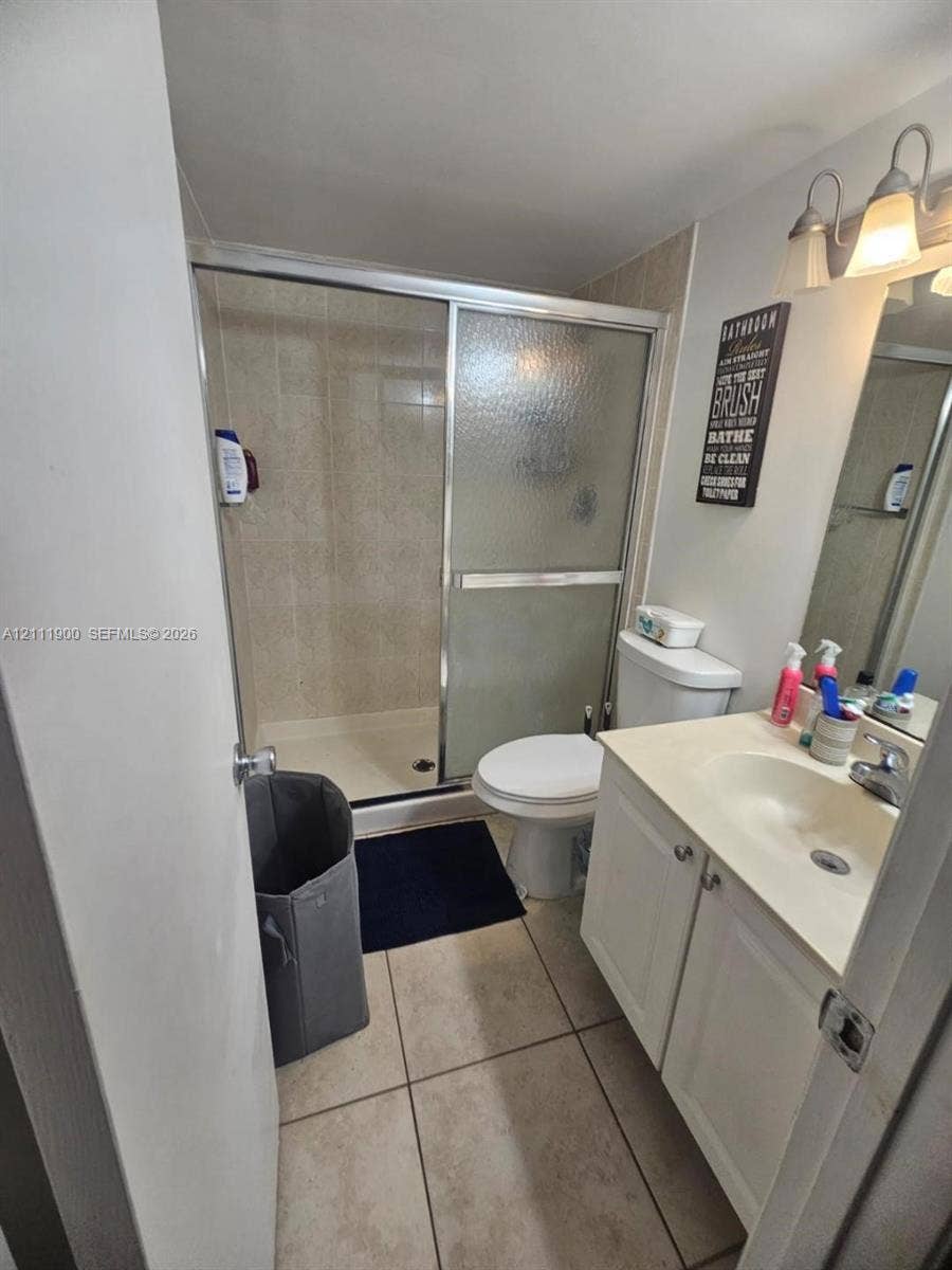 711 N Pine Island Road, #402, Plantation, Plantation, FL 33324 Bathroom featuring a walk-in shower with glass sliding doors, tiled flooring, a white vanity cabinet, and wall-mounted vanity lighting