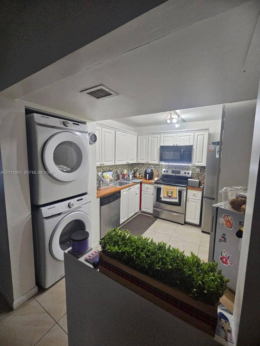 711 N Pine Island Road, #402, Plantation, Plantation, FL 33324 Kitchen featuring white shaker-style cabinetry, stainless steel appliances, tile flooring, and integrated laundry area