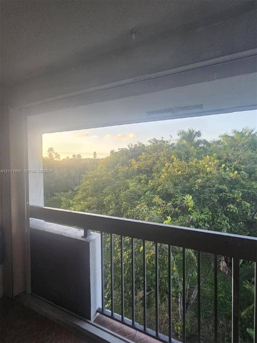 711 N Pine Island Road, #402, Plantation, Plantation, FL 33324 Covered balcony featuring dark metal railings, concrete wall supports, and tiling, oriented toward mature trees and foliage