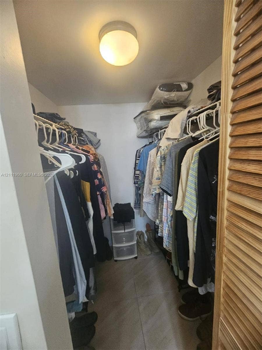 711 N Pine Island Road, #402, Plantation, Plantation, FL 33324 Storage closet featuring floor-to-ceiling shelving, hanging rods, tile flooring, and a flush-mount overhead light fixture, secured by wooden louvered doors