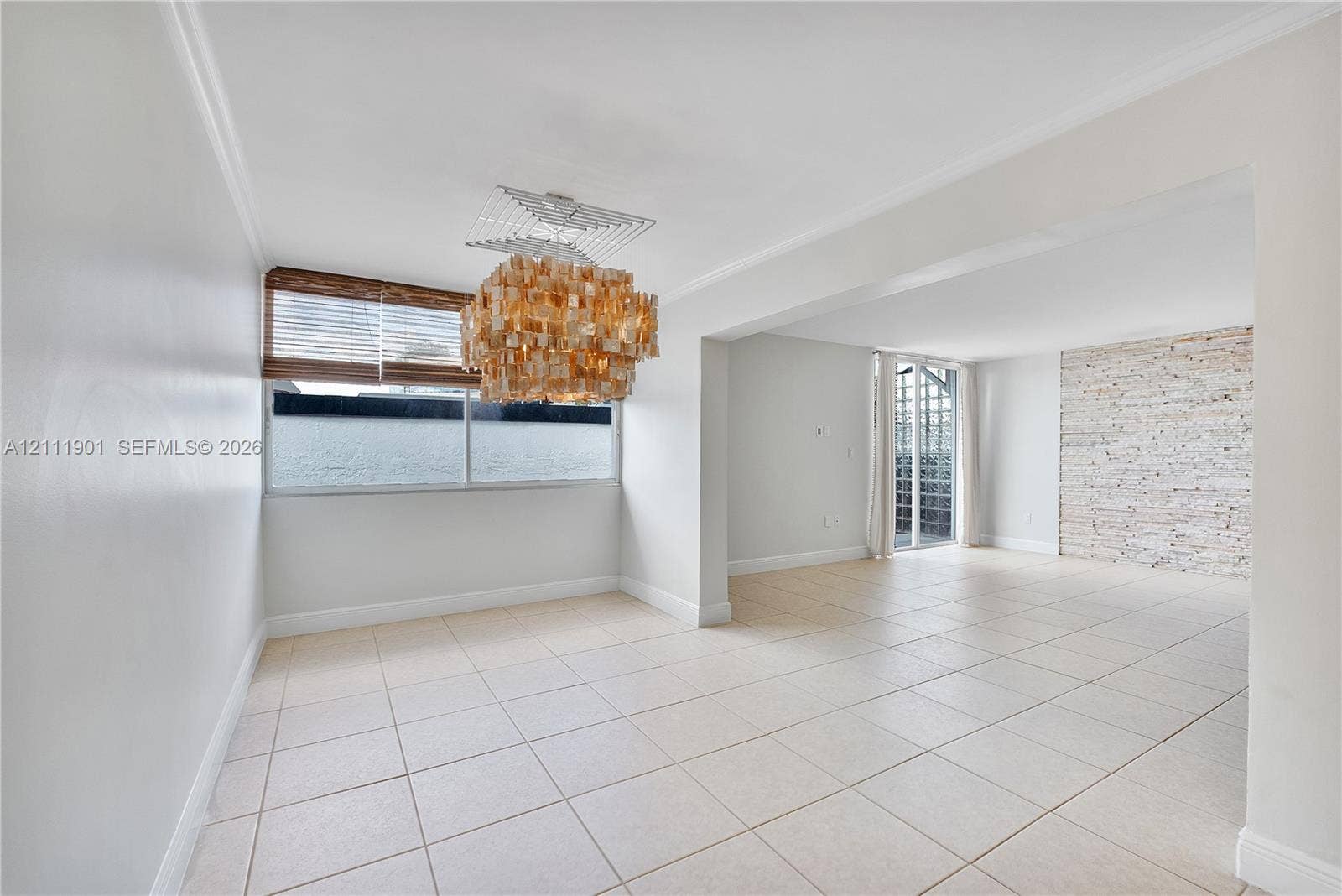 2977 Mcfarlane Road, #9, Miami, FL 33133 Open interior featuring large-format tile flooring, textured stone accent wall, multi-tiered crystal statement light fixture, and horizontal blind window coverings