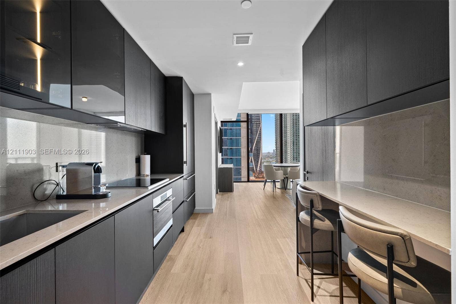 20 NE 11th Street, #4308, Miami, FL 33132 Kitchen featuring matte dark cabinetry, light-toned stone countertops, integrated appliances, wood-finish flooring, and a built-in breakfast bar