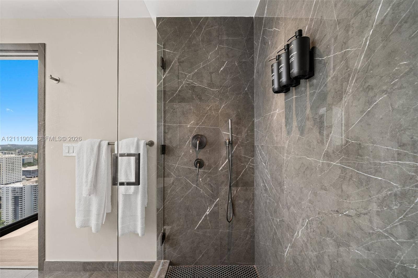 20 NE 11th Street, #4308, Miami, FL 33132 Walk-in shower featuring floor-to-ceiling stone-finish tile, frameless glass enclosure, dark-finish wall-mounted shower hardware, and mosaic tile flooring