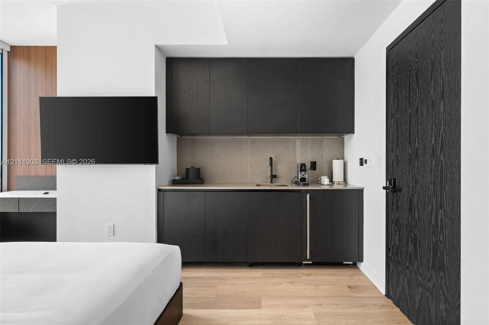 20 NE 11th Street, #4308, Miami, FL 33132 Wet bar featuring matte black cabinetry, stone-finish backsplash, undermount sink with matte black faucet, and built-in under-counter refrigerator