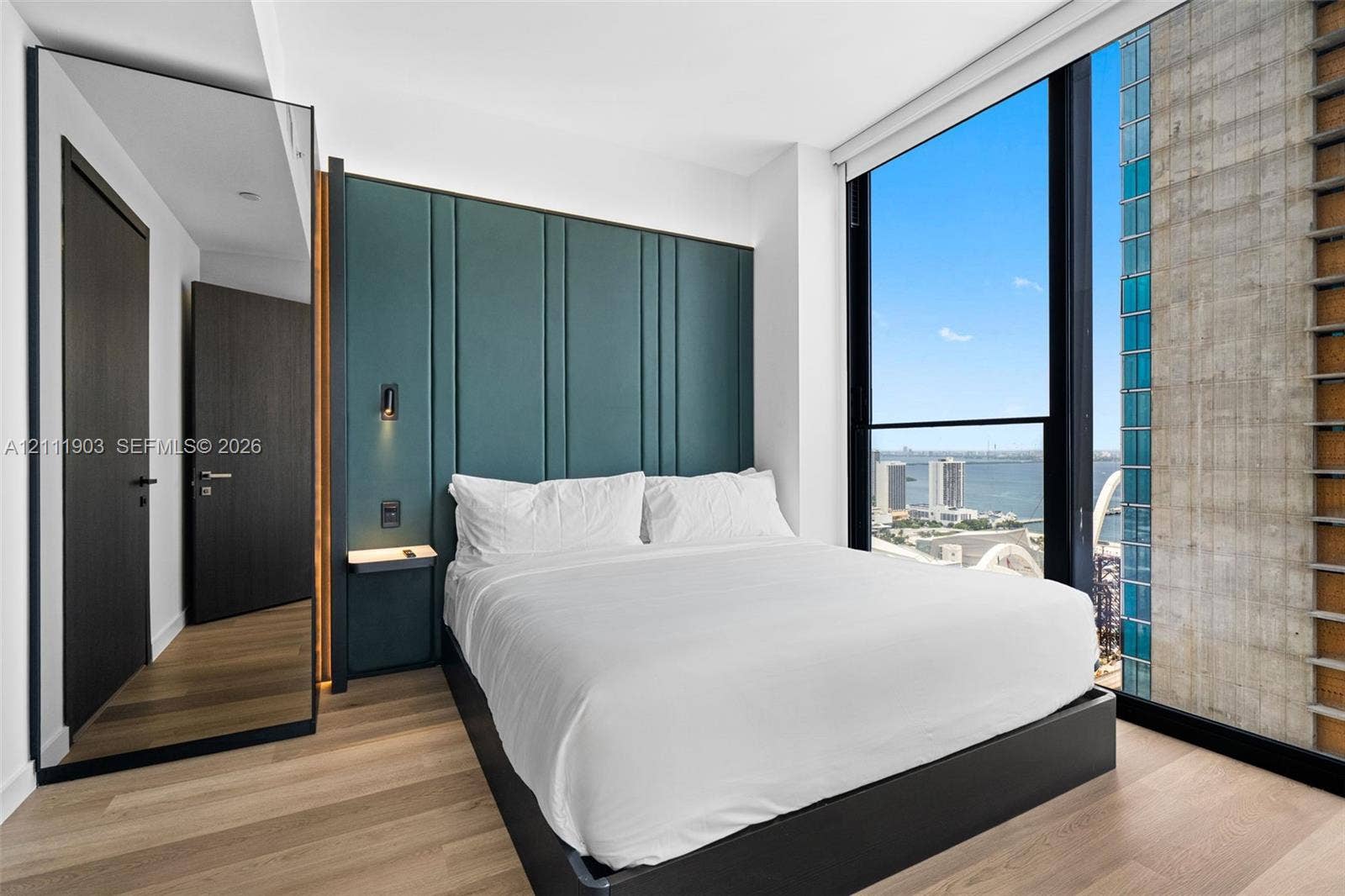 20 NE 11th Street, #4308, Miami, FL 33132 Floor-to-ceiling windows, custom teal paneling, wood-finish flooring, full-length mirror, and built-in wall-mounted bedside shelf