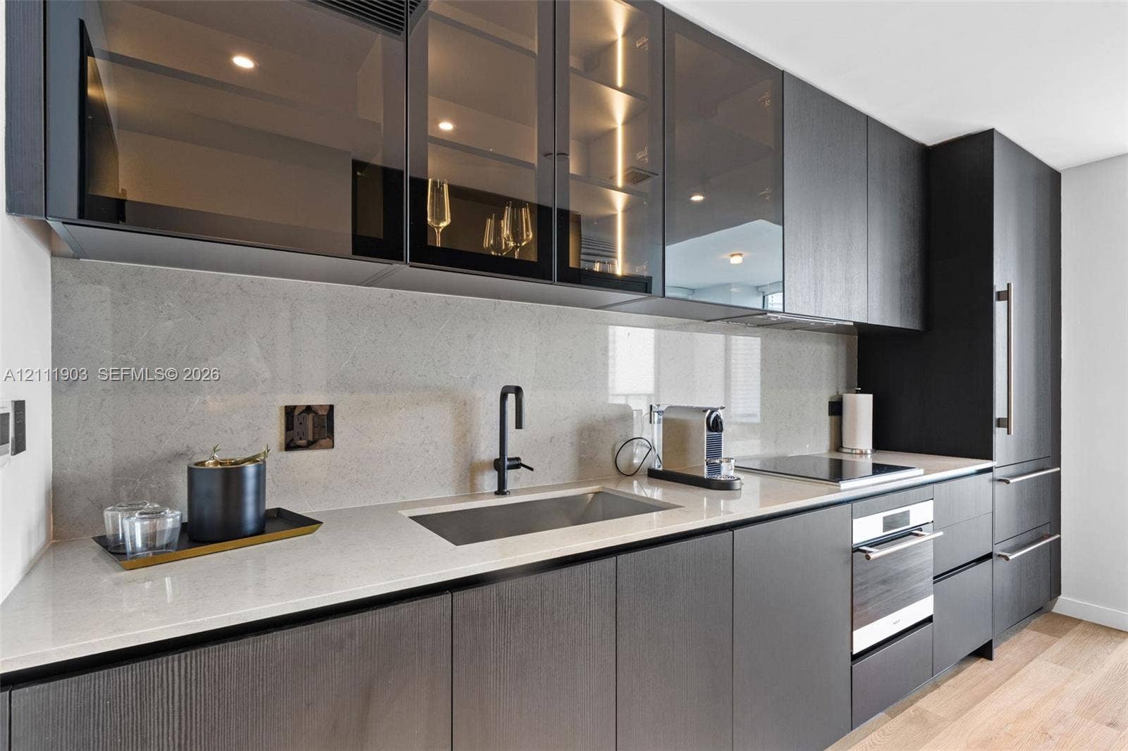20 NE 11th Street, #4308, Miami, FL 33132 Kitchen featuring flat-panel cabinetry with glass-front upper storage, light-toned stone-surface countertops, full-height backsplash, stainless steel undermount sink with matte black faucet, and built-in appliances