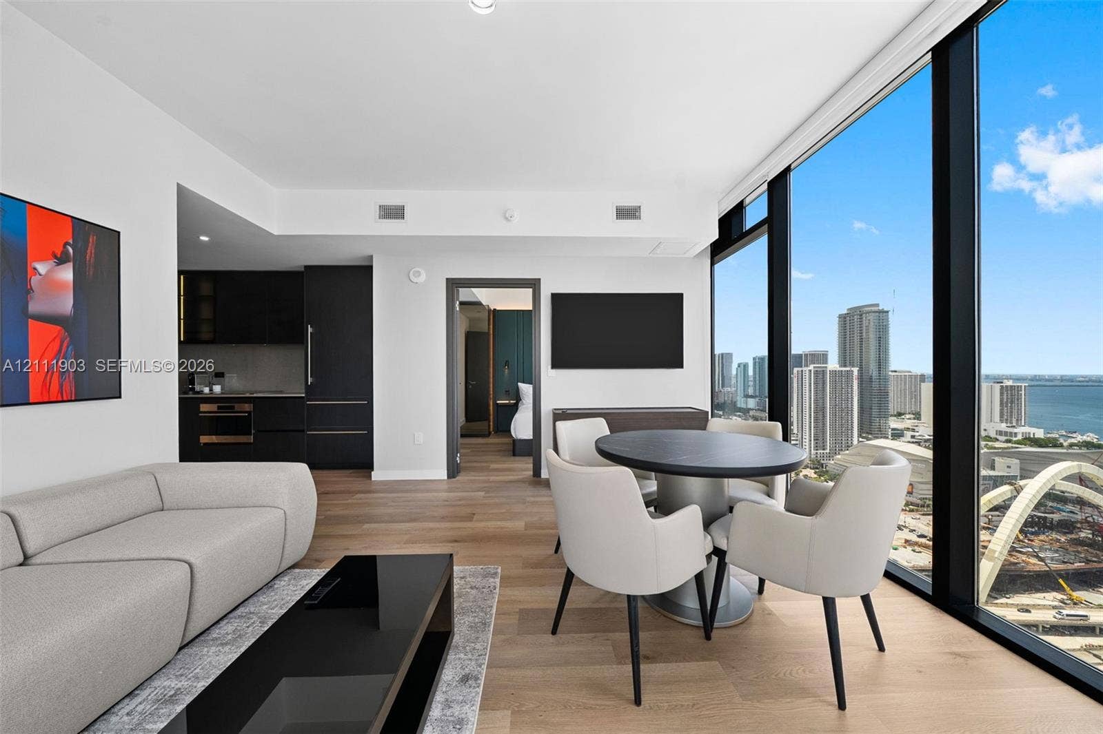 20 NE 11th Street, #4308, Miami, FL 33132 Floor-to-ceiling windows featuring panoramic city and water scenery, wood-finish flooring, and minimalist kitchen cabinetry with integrated appliances