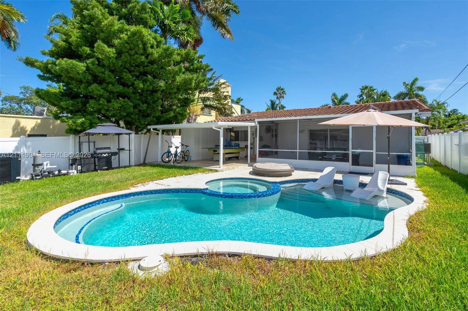 821 Harrison Street, Hollywood, FL 33019 Freeform swimming pool with a built-in spa, integrated sun shelf, screened-in lanai, and a fenced backyard